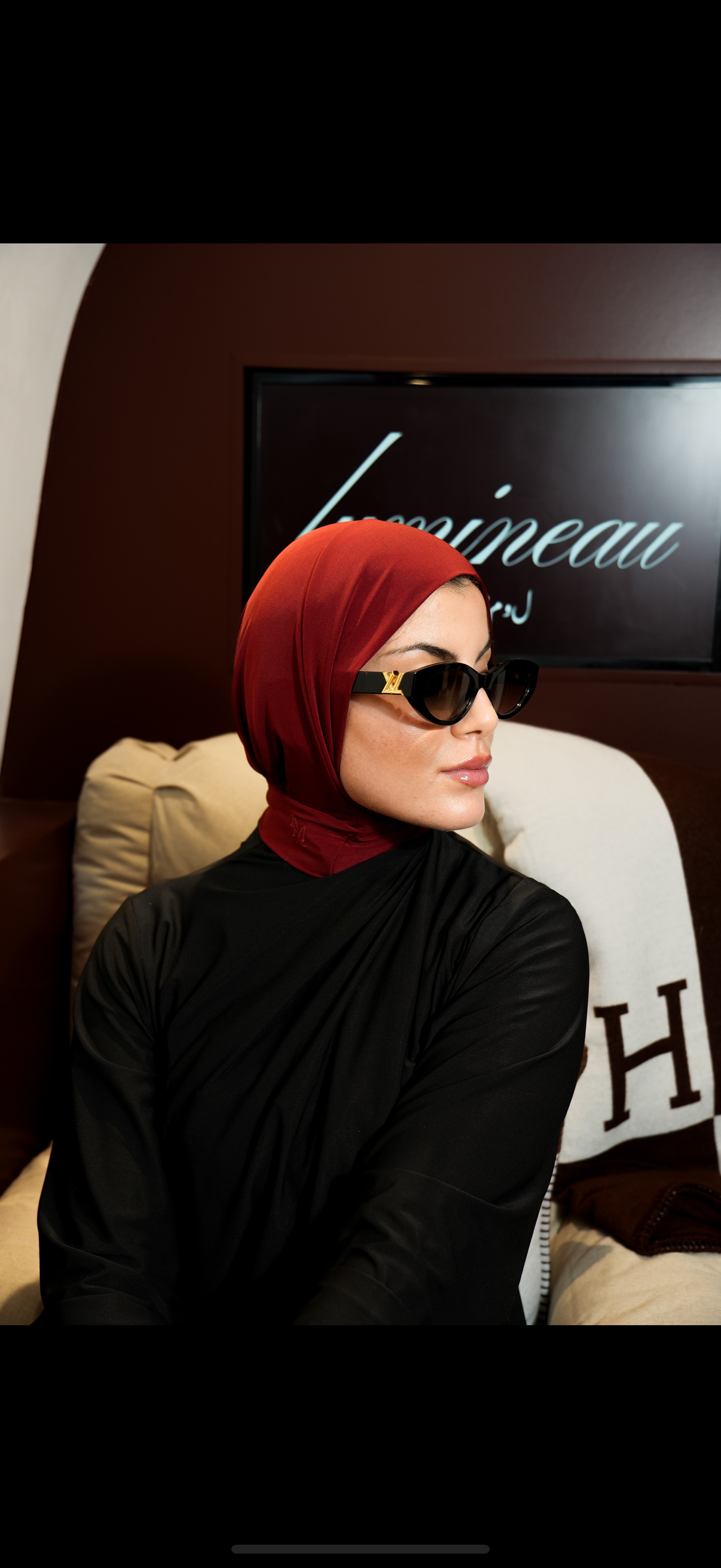 Woman wearing a red instant hijab and black outfit with sunglasses indoors.